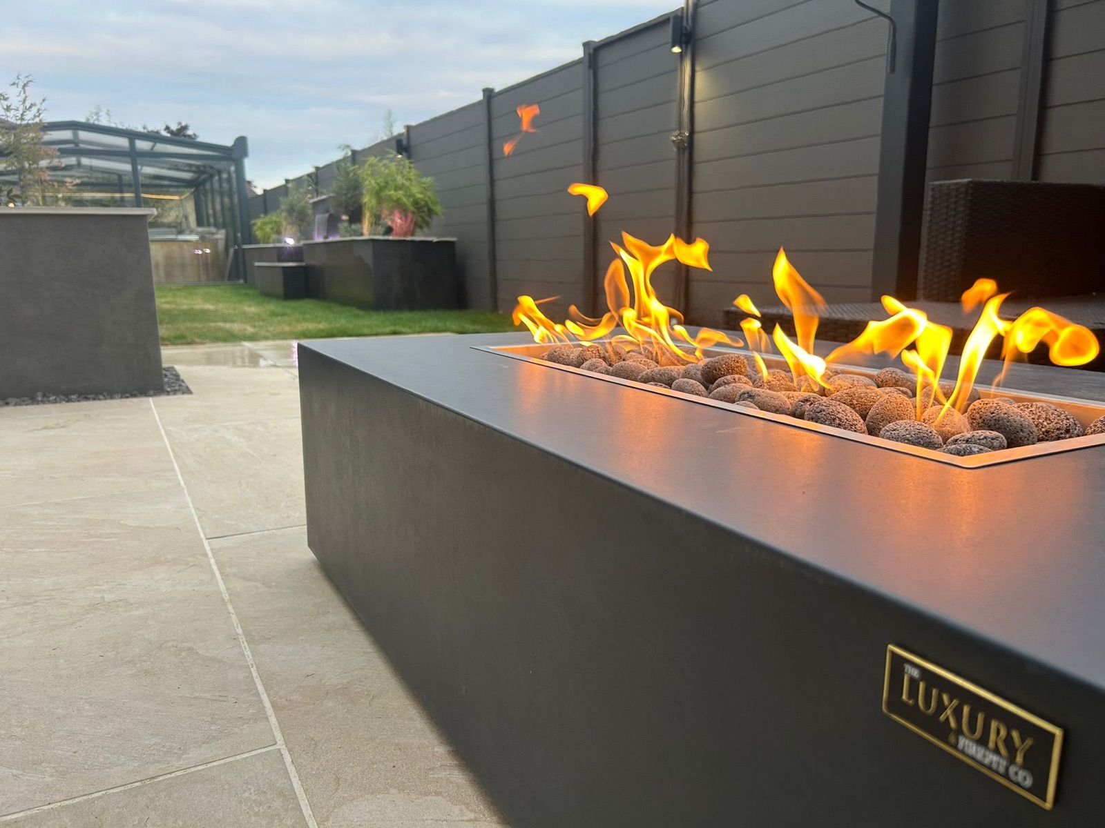 Linear gas fire pit with lava rocks burning at dusk on a porcelain patio