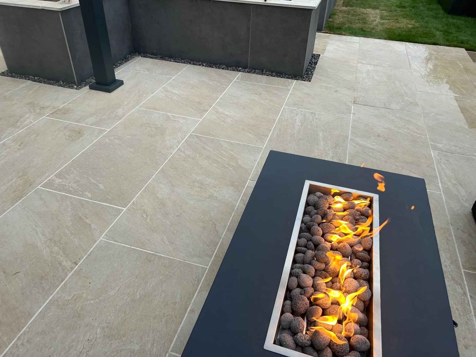 Porcelain-paved patio with built-in fire pit beside an outdoor kitchen island